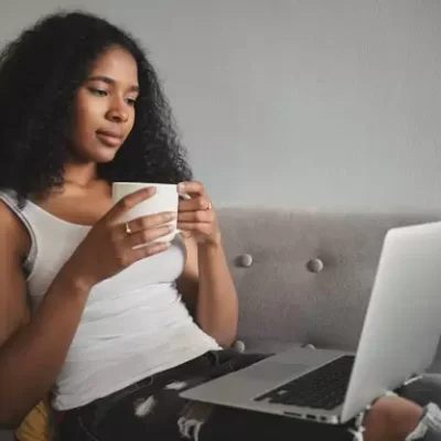 foto-de-lado-da-moda-jovem-atraente-de-pele-escura-em-jeans-rasgados-relaxando-no-sofa-com-o-computador-portatil-no-colo-bebendo-cafe-e-assistindo-a-serie-de-tv-favorita-online_343059-1584